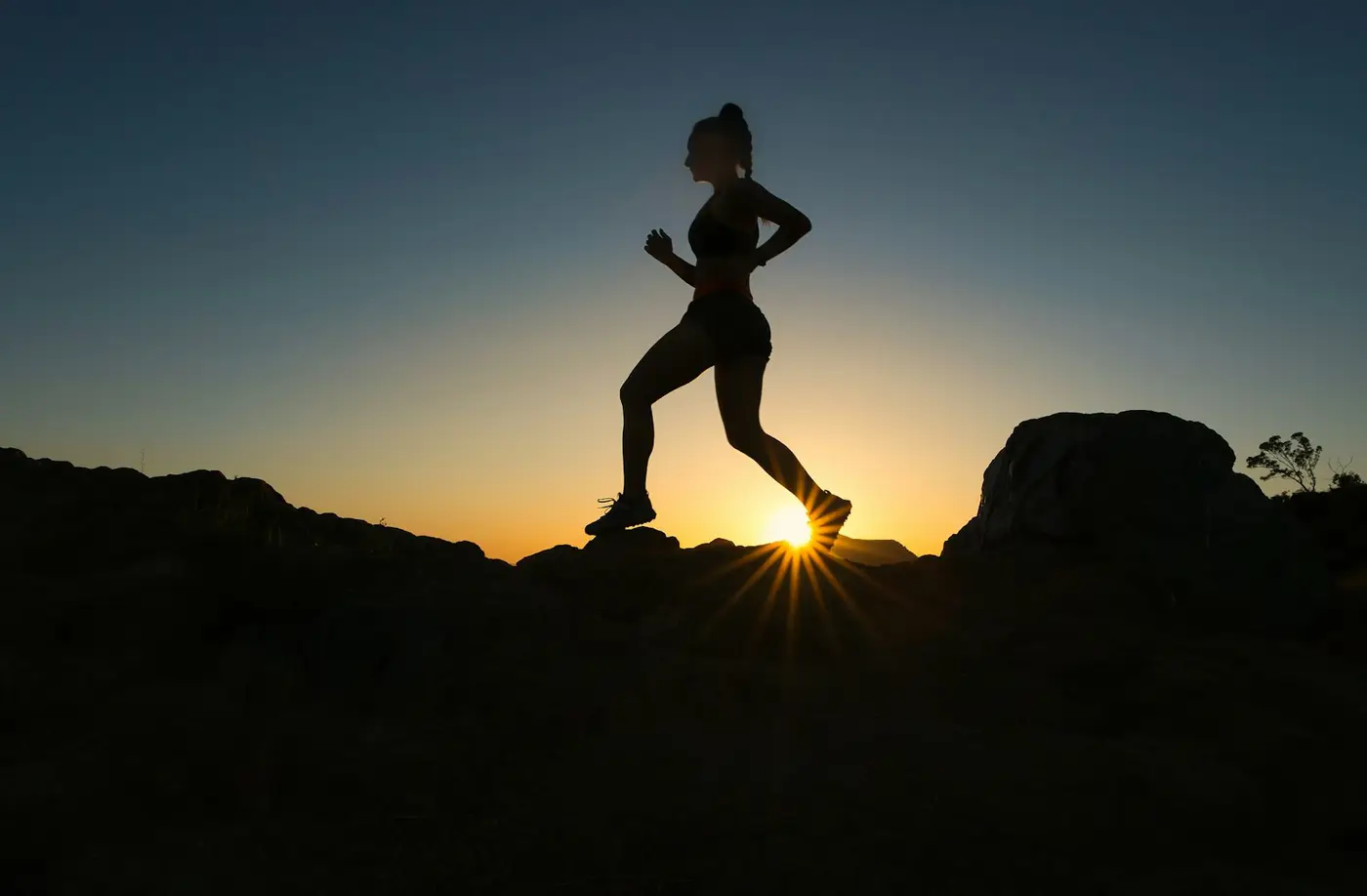 Läuferin als Silhouette auf dem Trail, tiefe Sonne