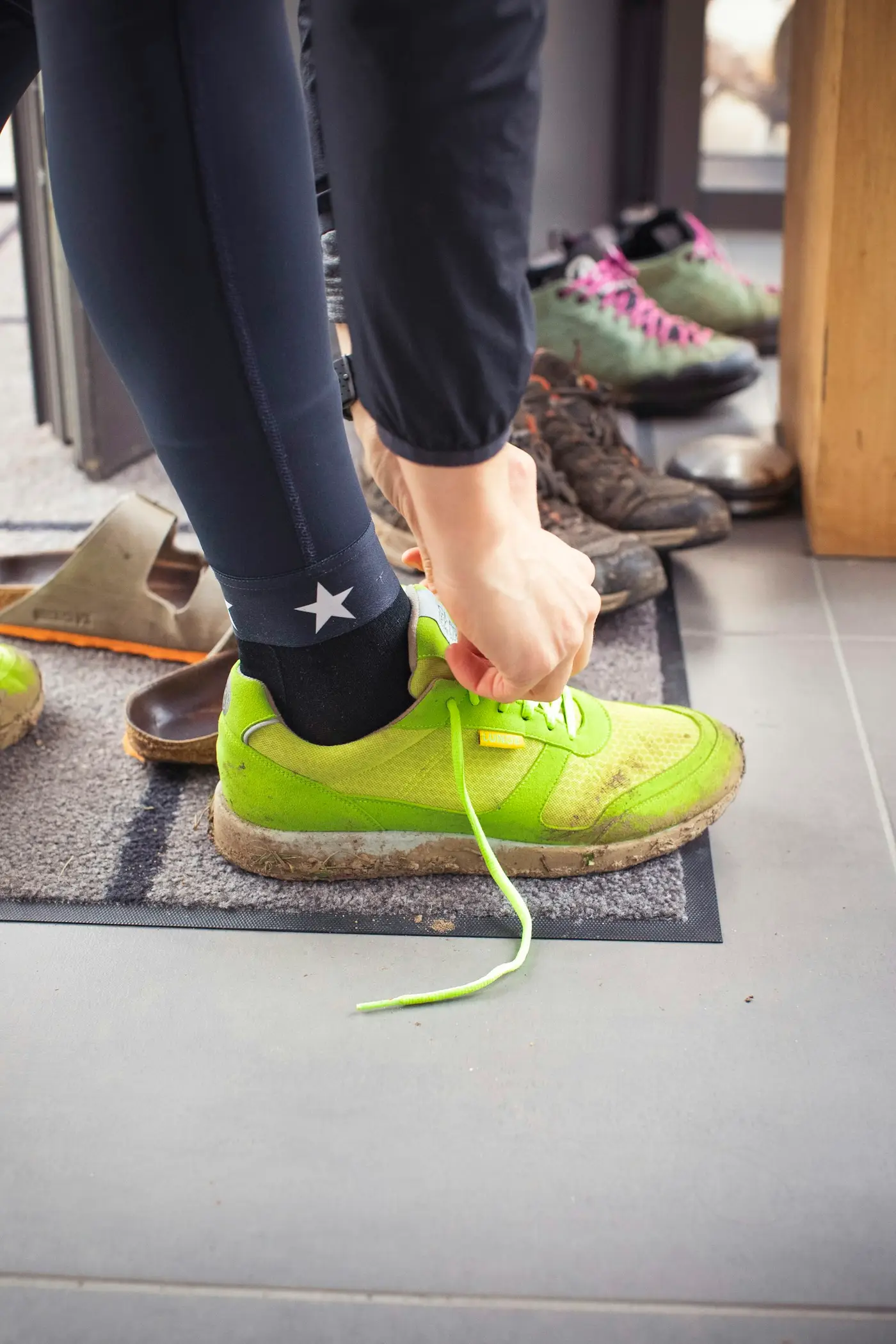 Laufschuh wird auf der Fußmatte im Hausflur gebunden, daneben andere Schuhe